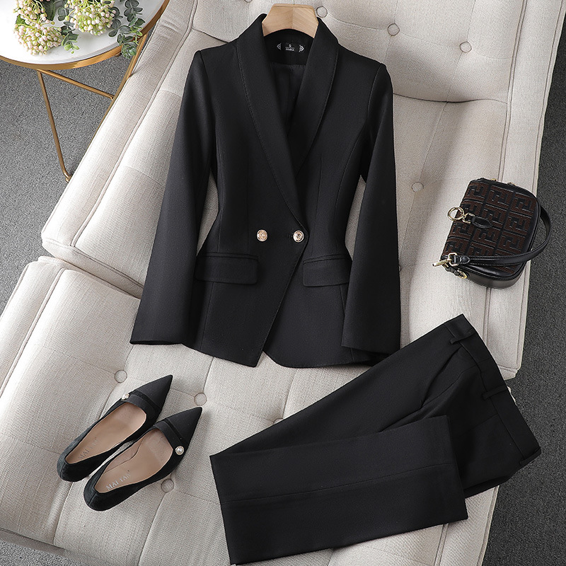 Ein schwarzer Blazer und eine passende Hose, arrangiert auf einer weichen Unterlage, begleitet von spitzen schwarzen Pumps und einer kleinen Handtasche.